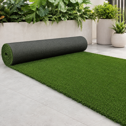 A roll of green artificial turf or grass carpet partially unrolled on a light gray tiled floor, with potted plants in the background.