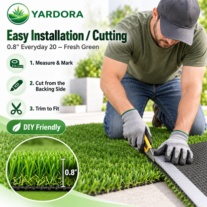 A man kneels on a green artificial turf lawn, using a utility knife to cut a roll of Yardora 0.8" fresh green turf.