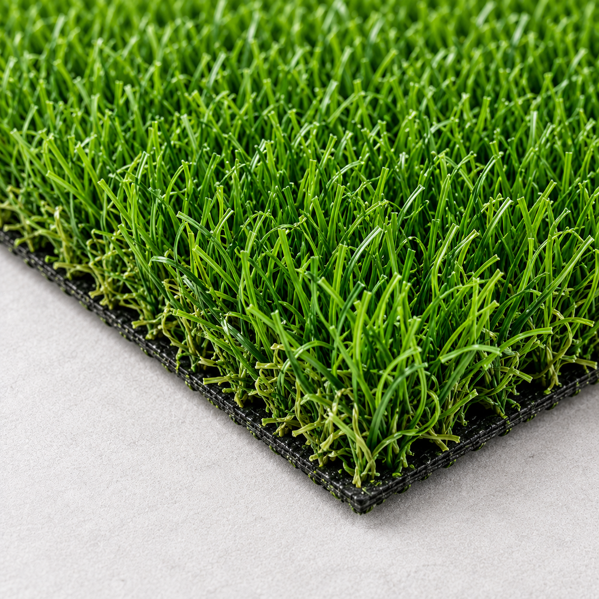Close-up of bright green artificial turf with dense grass-like strands on a black backing, shown on a light gray surface.